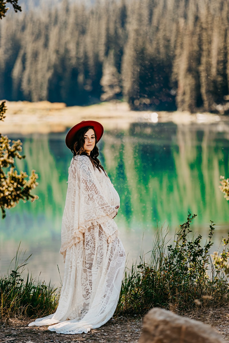 Maternity Photographer, a young mother holds her belly, she is pregnant and stands near a forest lake