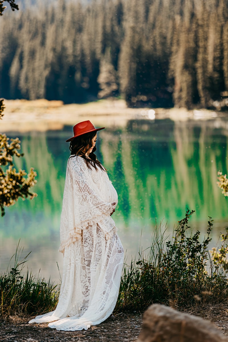 Maternity Photographer, a young pregnant woman in white gown stands at lake shore