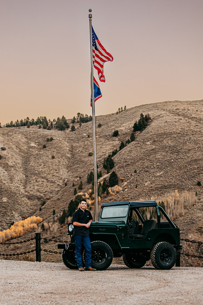 Senior Photographer,  a high school aged man stands next to a jeep and an American Flag