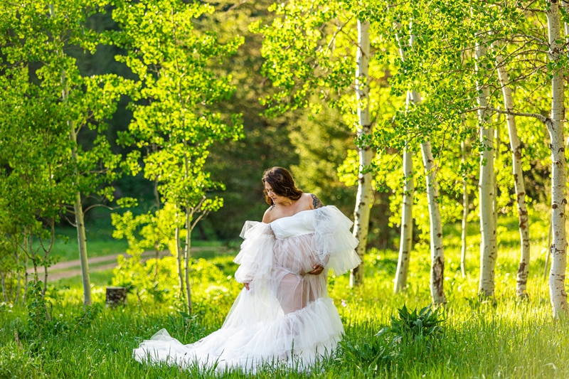 Maternity Photographer, a pregnant mother wears a white gown and walks in a near aspens