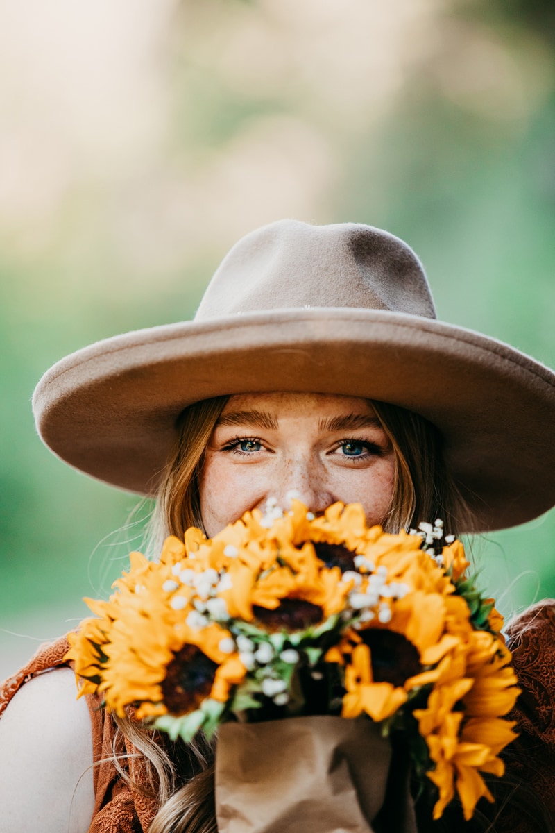 Senior Photographer, a woman with joy inn her eyes hides behind sunflowers