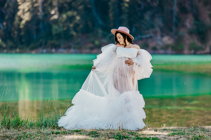 Maternity Photographer, a pregnant woman in white dress stands before lake