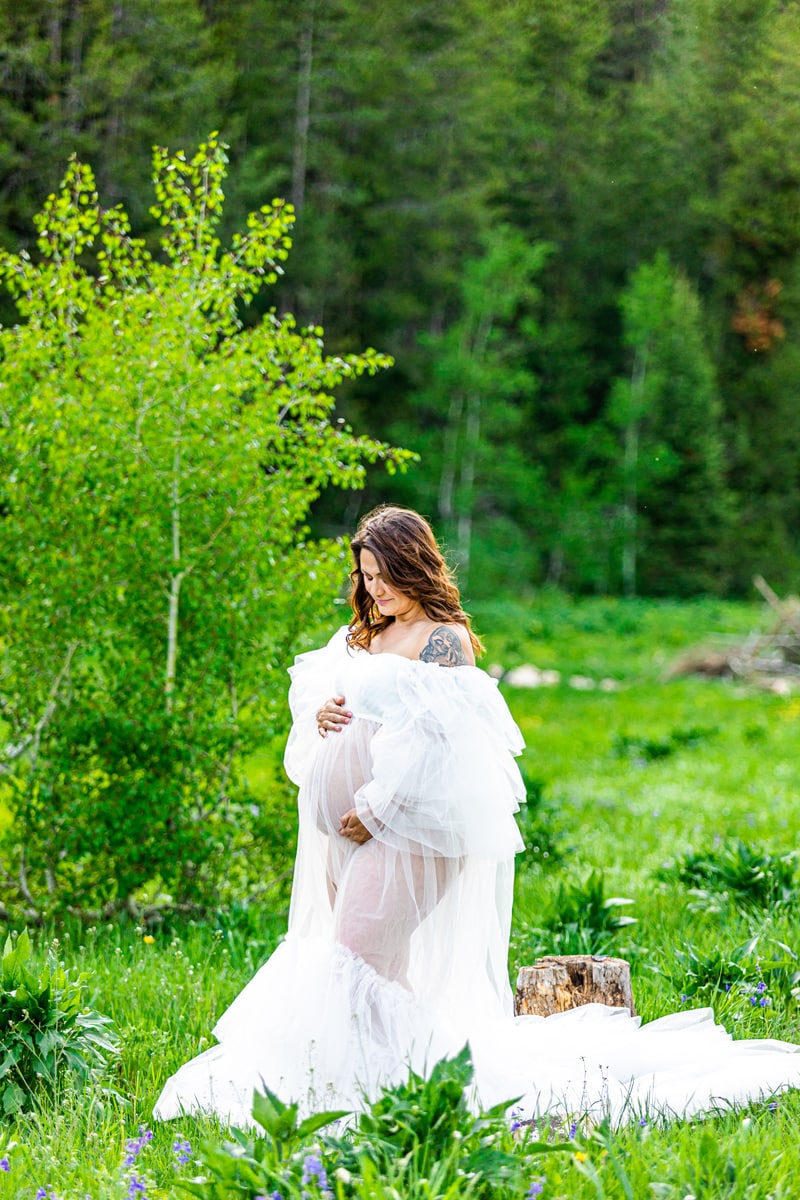 Maternity Photographer, a mother wears a white gown and stands a grassy meadow