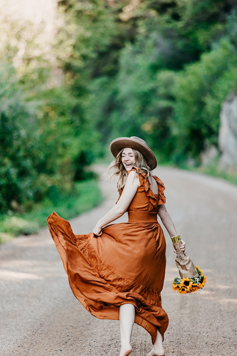 Senior Photographer, a high school girls skips happily with her dress and flowers in hand
