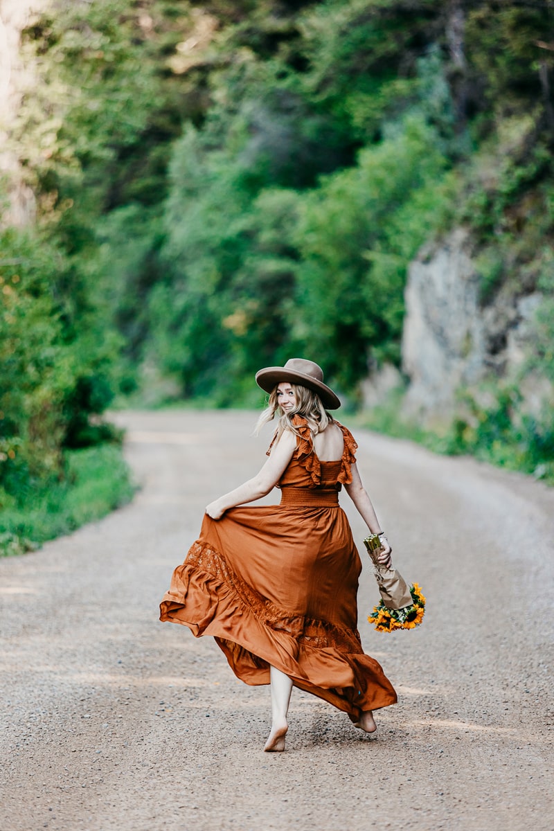 Senior Photographer, a young woman skips down a country road with a smile