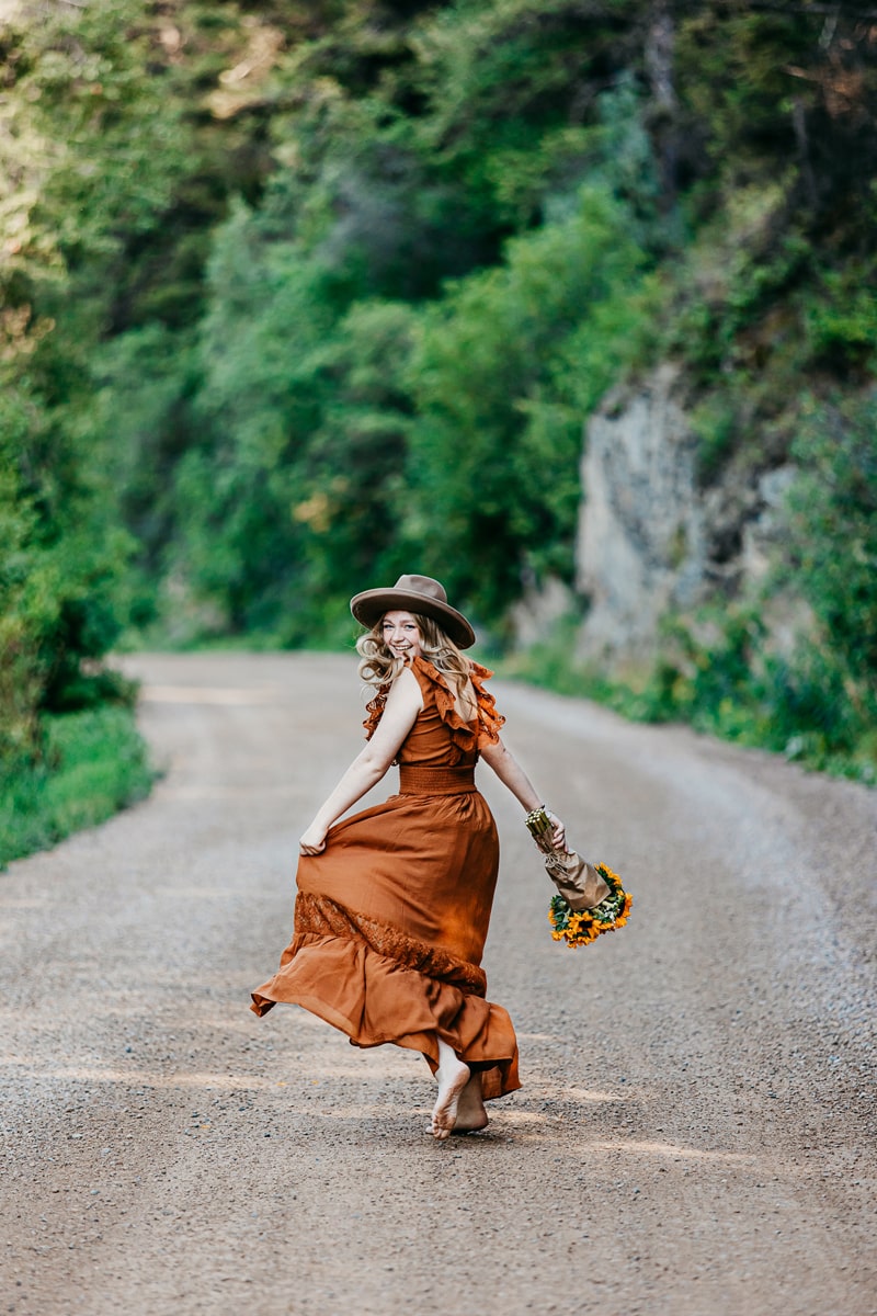 Senior Photographer, a high school aged woman smiles and runs down a country road in a dress