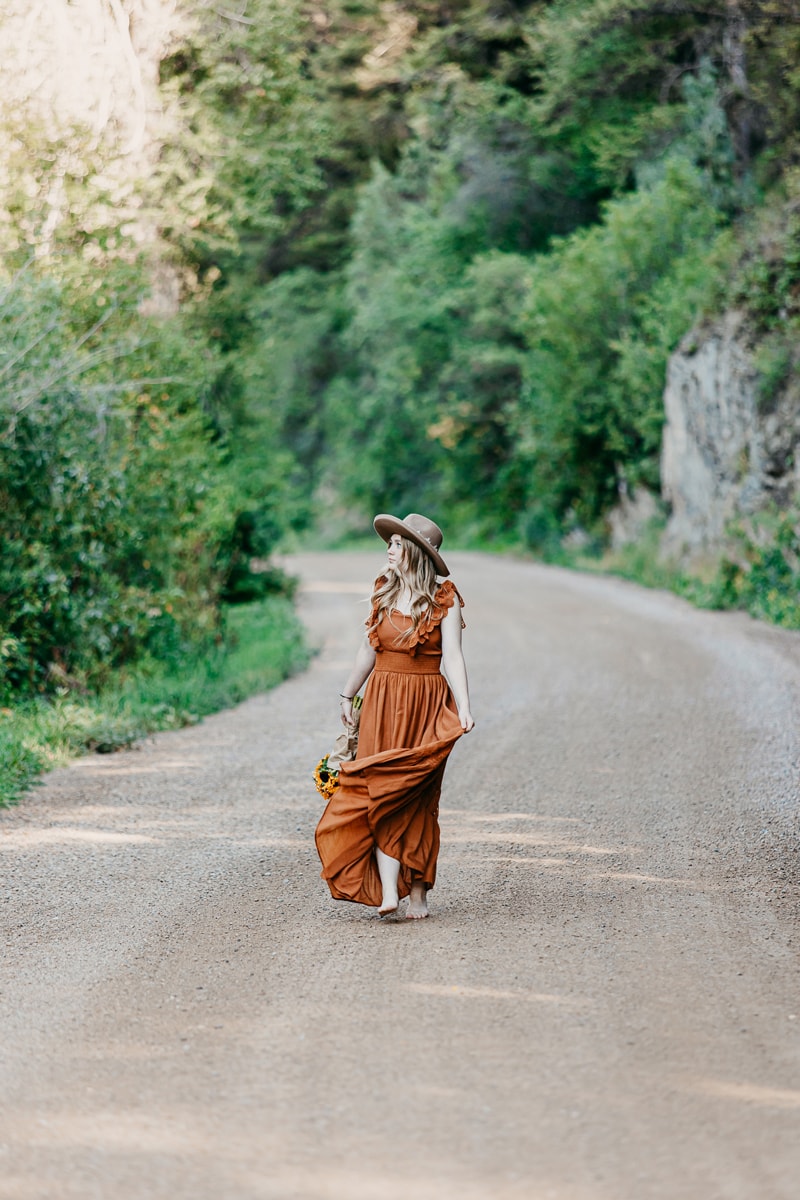 Senior Photographer, a high school girl holds her flowing dress as she admires the outdoors