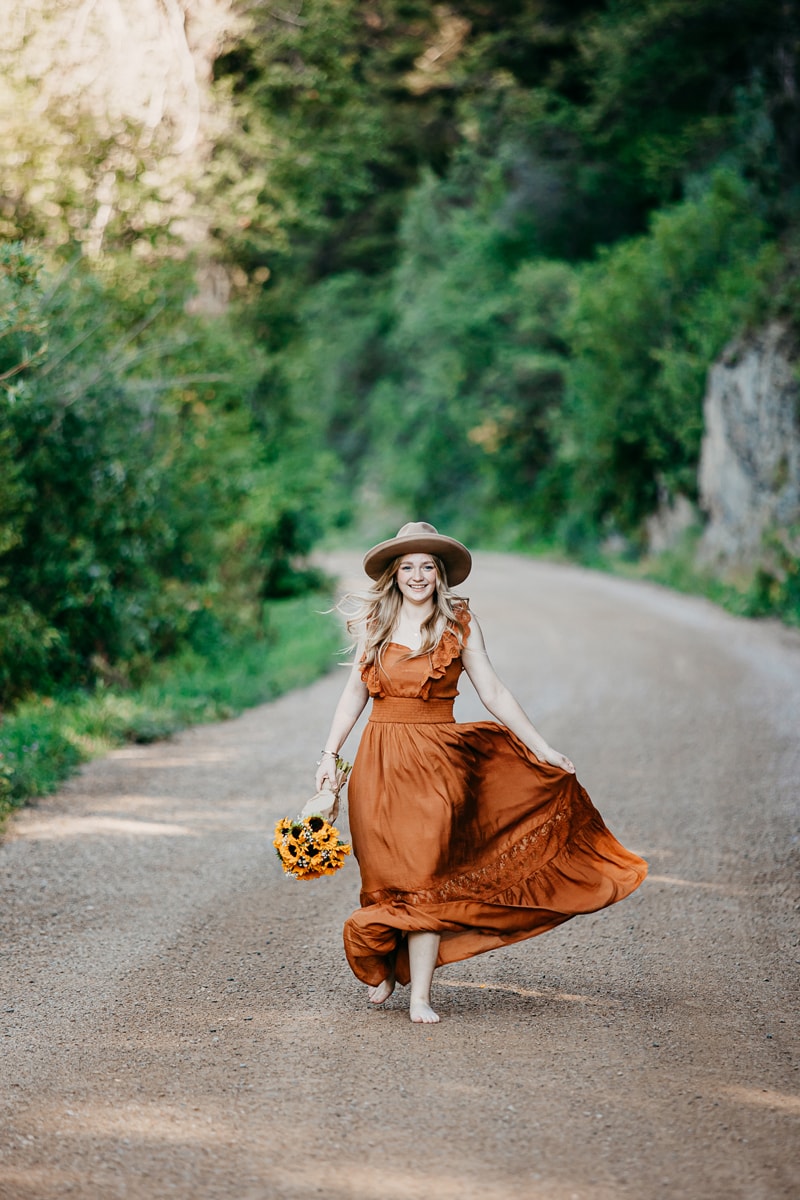 Senior Photographer, a girl holds her dress and flowers as she walks down a country road