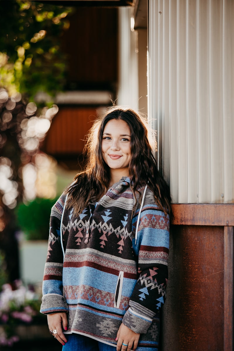 Senior Photographer, A high school girl wears a. jacket with native American patterns and smiles