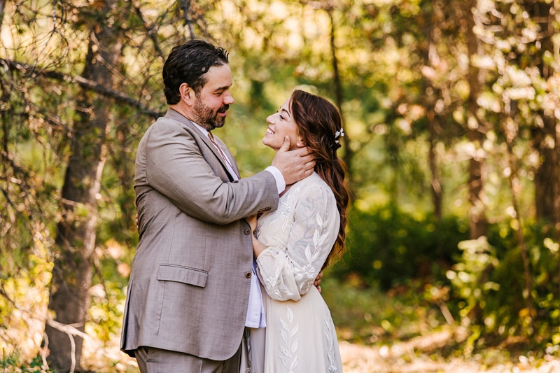 Wedding Photography, a happy husband and wife hold each other beneath the forest trees on a sunny day