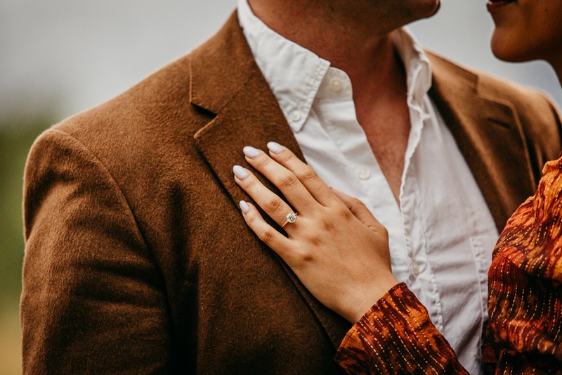 Couples photographer, a woman's hand with wedding ring is on her husband's chest, he wears a coat