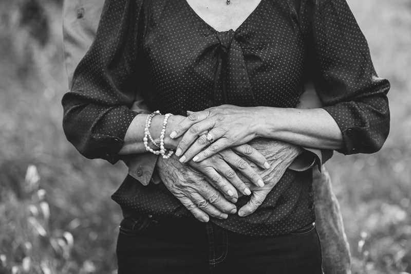Couples Photographer, wrinkled hands embrace a woman from behind, her hands hold his