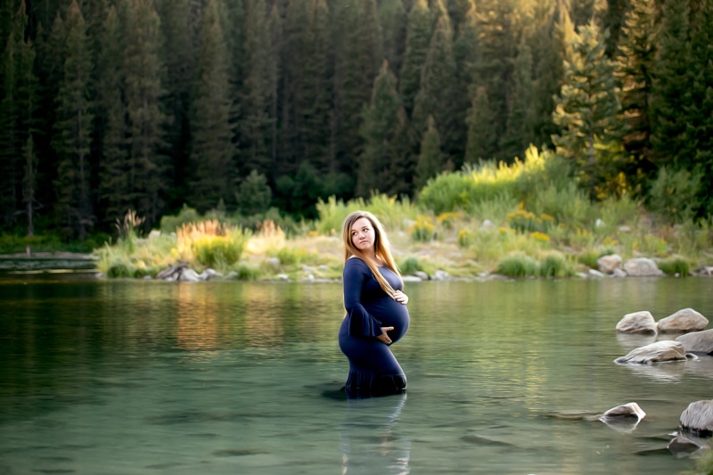 Maternity Photographer, a young mother-to-be wears a blue maternity gown and stands in lake waters