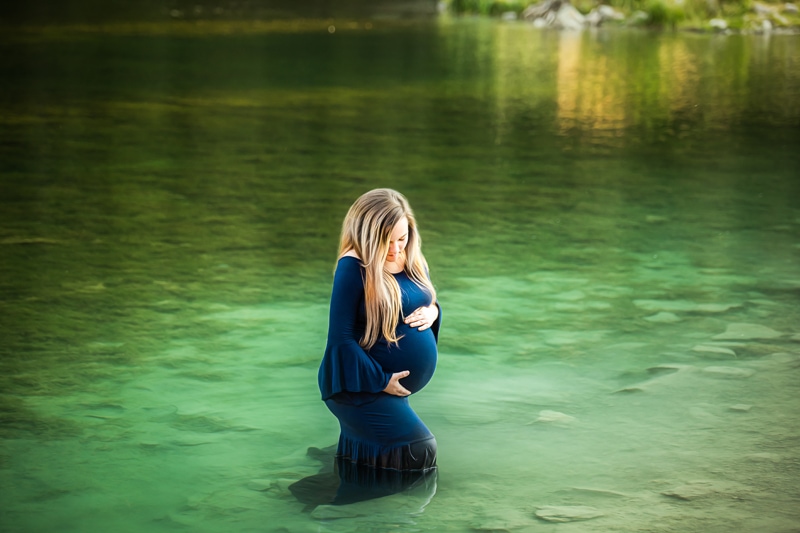Maternity Photographer, a young pregnant mother holds her belly as she stands in shallow lake waters
