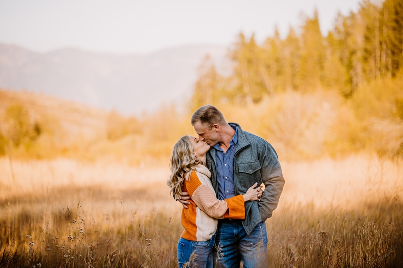 Couples photographer, a husband and wife kiss as they stand together in a dry meadow