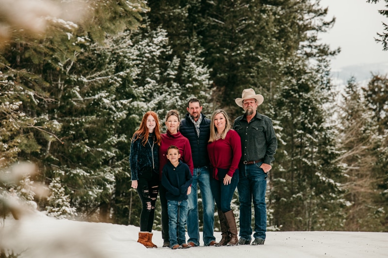 Family Photographer, a mom, dad, grandparents, son, and daughter, stand in the snow covered woods