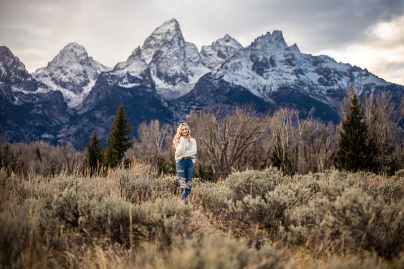 Senior Photographer, a woman stands in the wilderness before chaparral and snow topped mountains