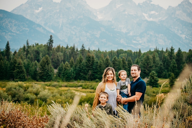 Family Photographer, a mom and dad stand with their boys in the woods