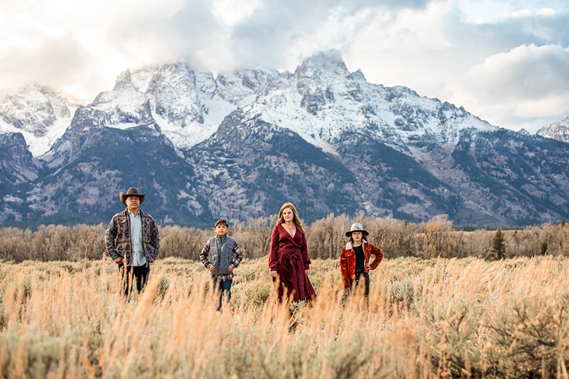 Family Photographer, a father, mother, and two sons stand in a dry meadow before the snowy mountains