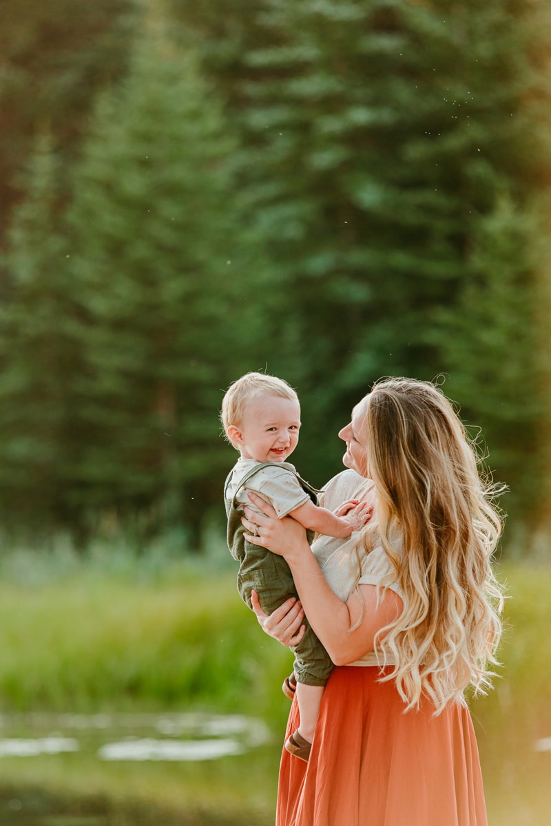 Family Photographer, a young mother holds her baby smiling baby boy in the forest