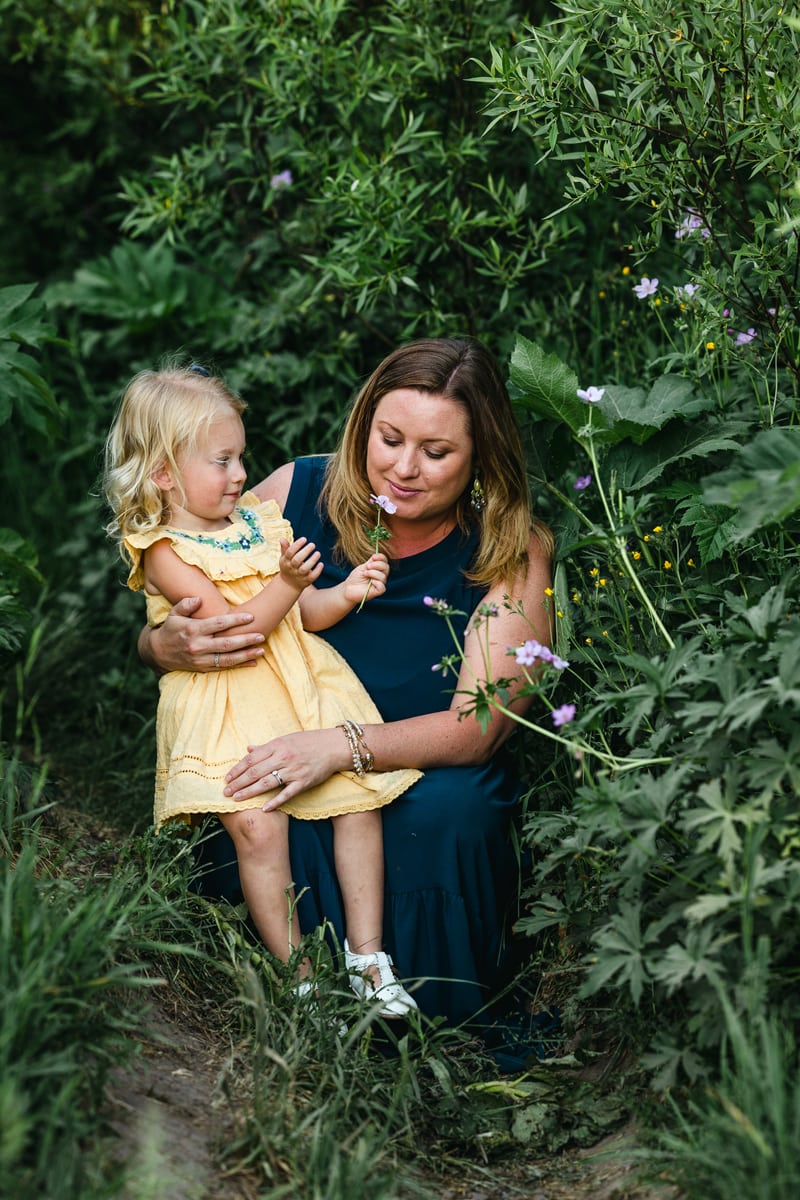Family Photographer, a mother embraces her daughter who shows her a wildflower
