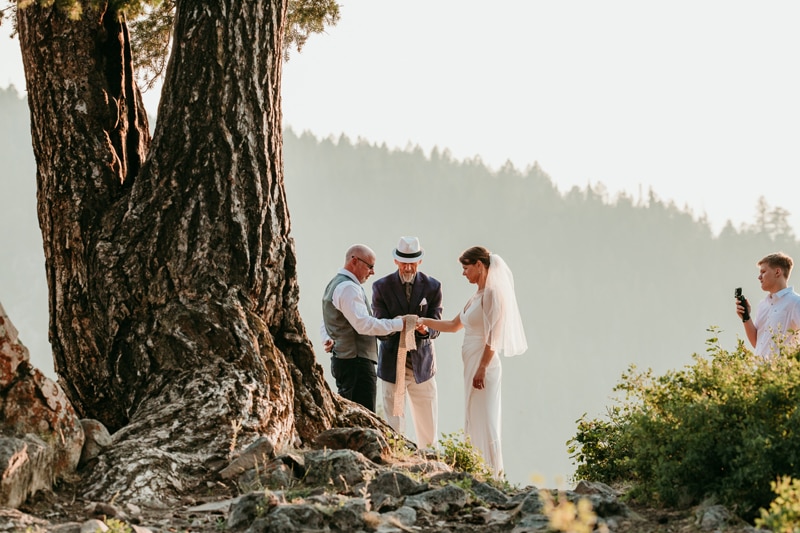 Family Photographer, a wedding is being performed in the mountains near a large tree, they are eloping
