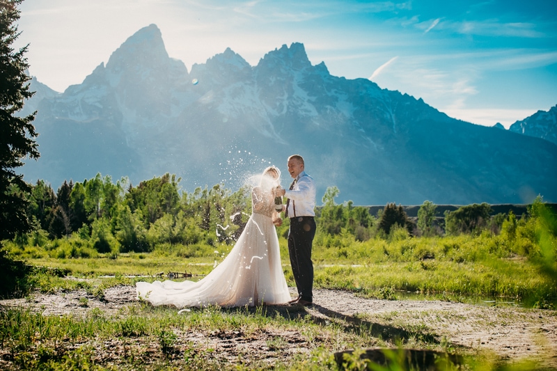 Wedding Photography, bride and groom pop open a bottle of champagne in the mountains