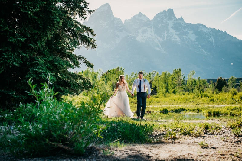 Wedding Photography, a bride and groom hold hands as they walk beneath the vibrant green landscape, the mountains behind them