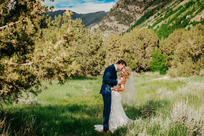 Wedding Photography, a groom kisses his bride in the grassy meadows at the foot of the mountainside