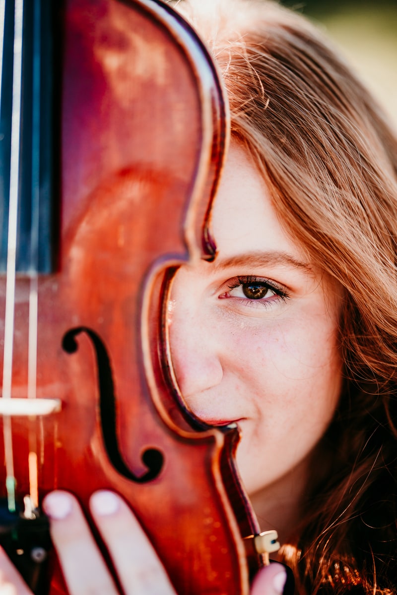 Senior Photographer, a high school girl looks happy as she hides behind her violin