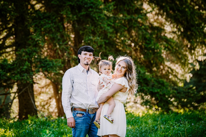 Family Photographer, a young mom and dad hold their baby daughter with pig-tails in her hair
