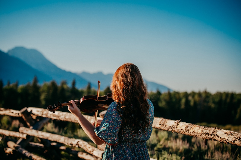 Senior Photographer, woman plays violin in mountain meadows