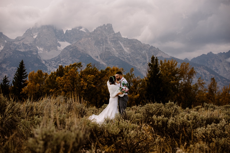 Wedding Photography, a young husband and wife kiss with the mountains and forest behind them