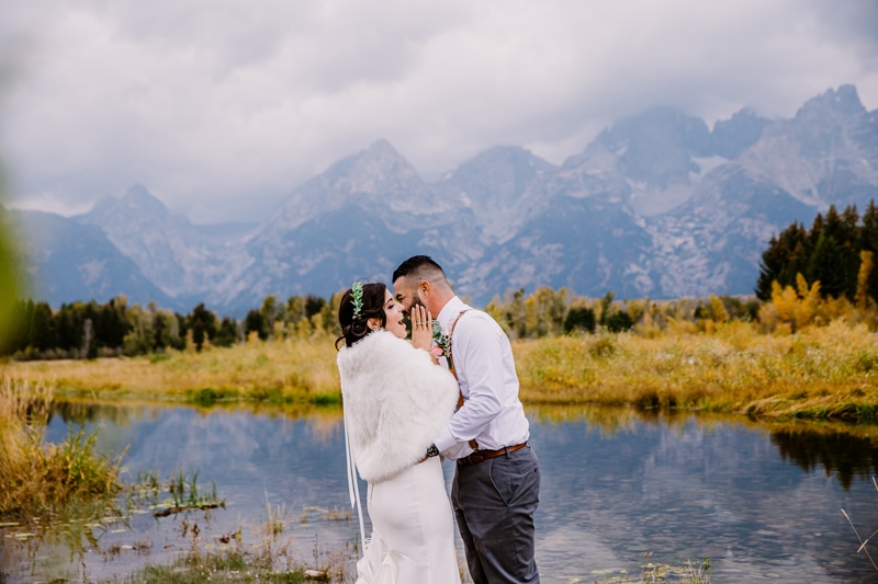 Wedding Photography, a groom leans into his bride as she laughs as the stand before quiet streams in the mountain wilderness