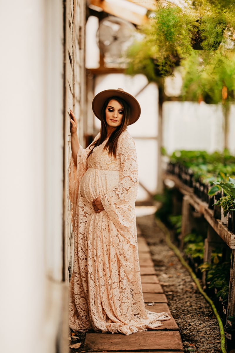 Maternity Photographer, a young mother-to-be wears a maternity gown and stands near a home vegetable garden