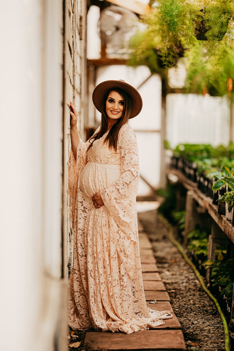 Maternity Photographer, a young woman in a maternity gown stands on a stone path in a garden