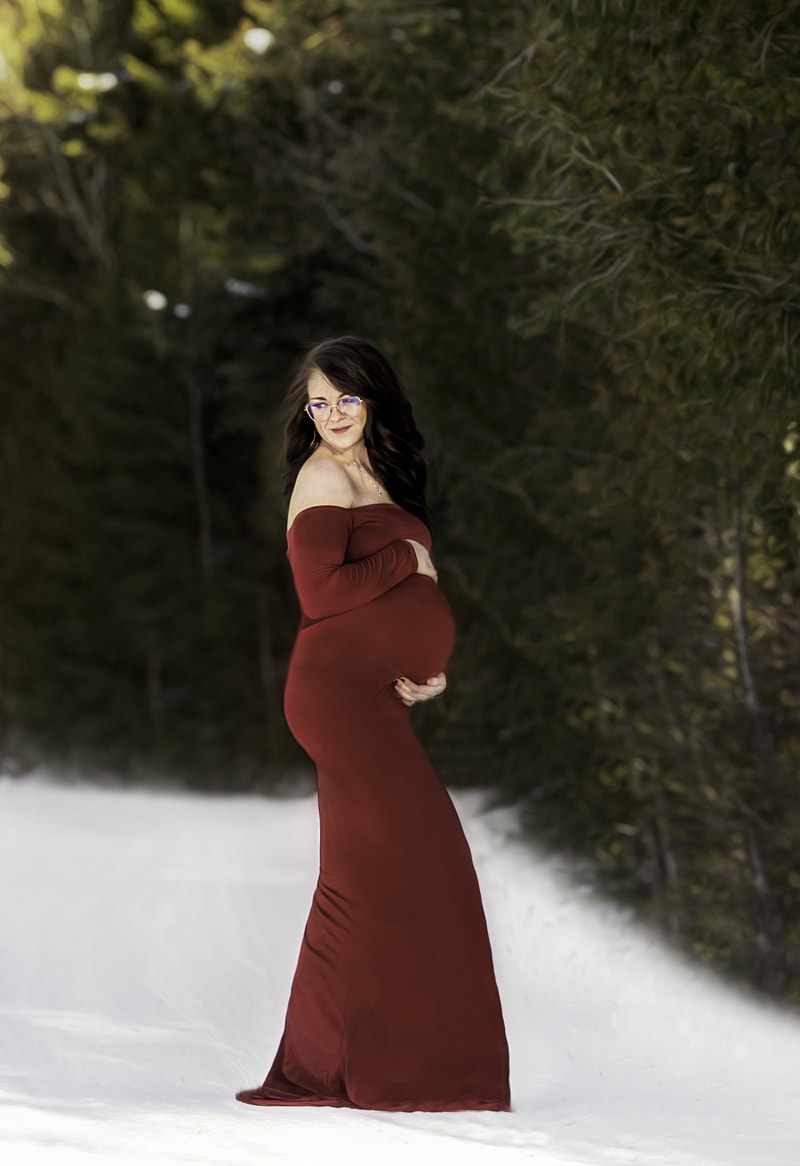 Maternity Photographer, expecting mother stands in snow near forest